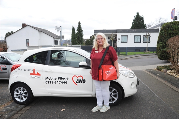 Eine Mitarbeiterin steht vor einem weissen Auto. Das Auto trägt die Aufschrift Mobile Pflege und zeigt das Logo der Arbeiterwohlfahrt.