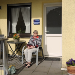 Eine Seniorin sitzt in der Sonne auf der Veranda ihrer Wohnung