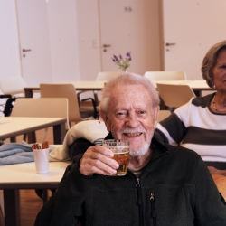 Zwei ältere Menschen trinken Kaffee und lachen in die Kamera.